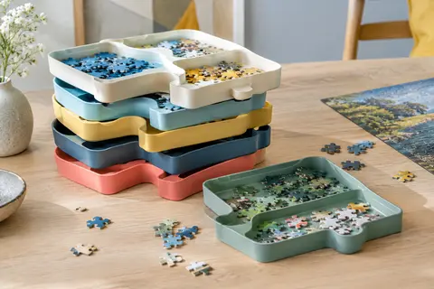 Six plateaux de tri multicolores empilables avec des pièces de puzzle sur une table en bois clair