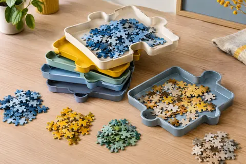 Six plateaux de tri pour puzzle en plastique aux teintes variées, empilés sur une table avec des pièces classées.